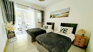 A double bed room with a view of the outdoors, a painting on the wall, and a nightstand with a lamp.