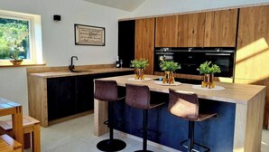 A modern kitchen with wooden cabinets, a central island with bar stools, and potted plants.