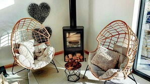 Two wicker chairs with cushions, a black wood-burning stove, and a heart-shaped wall decoration.