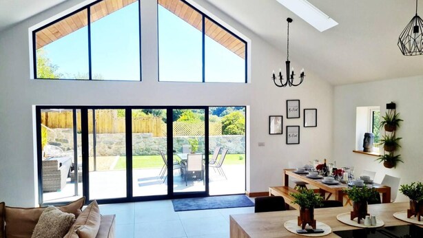 A spacious living area with a large sliding glass door leading to a backyard, a dining area with a wooden table set for four, and a modern chandelier.