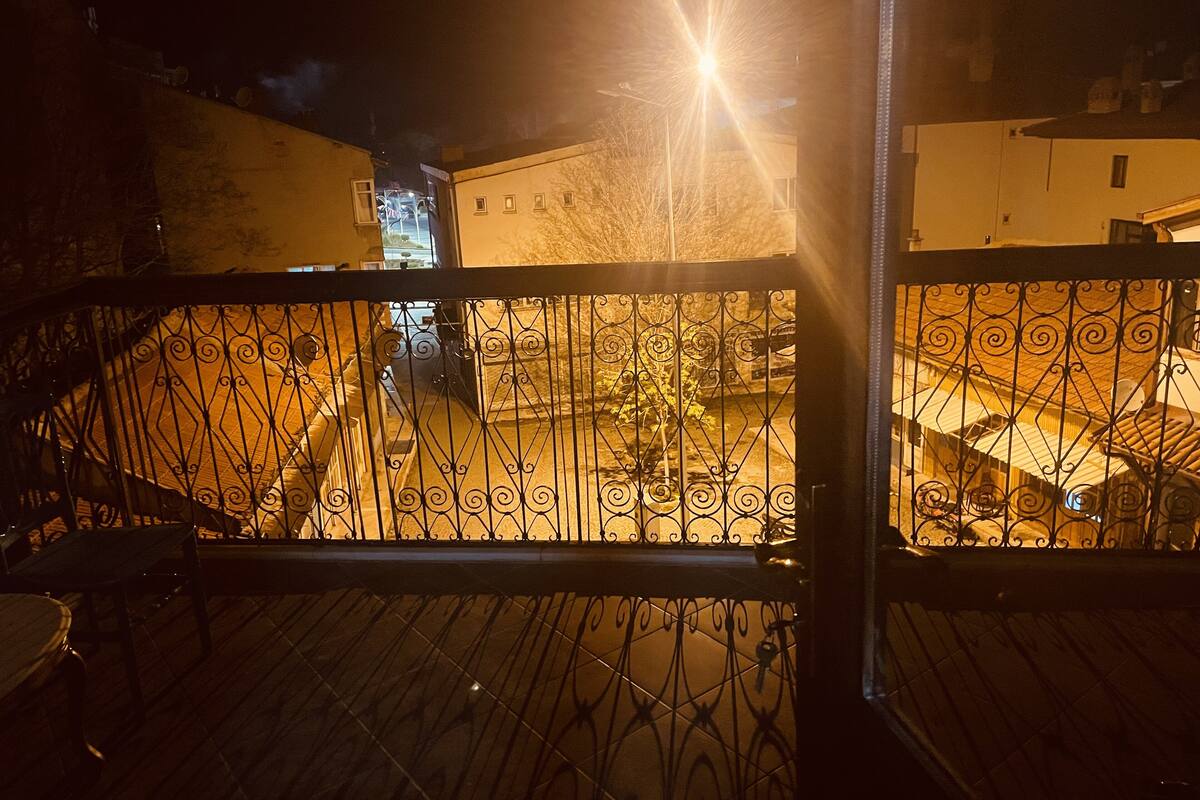 A nighttime view from a balcony with a wrought iron railing, overlooking a courtyard with a staircase and a building in the background.