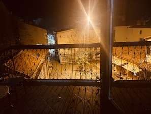 A nighttime view from a balcony with a wrought iron railing, overlooking a courtyard with a staircase and a building in the background. - Küçükağa Konağı (Aksehir)