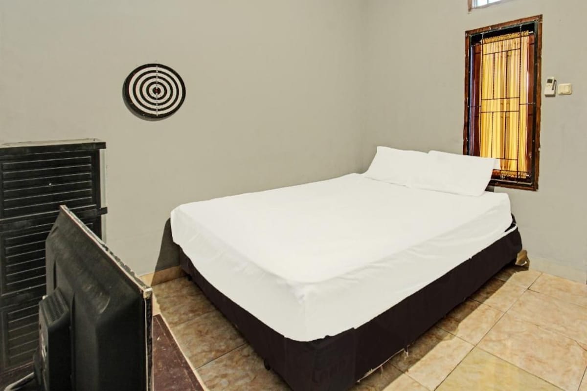 A single bed with a white mattress and black frame, a wall-mounted target, a radiator, and a window with curtains.