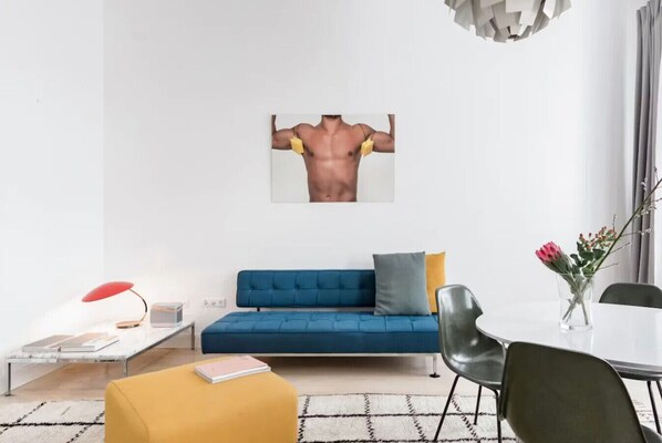 A modern living room with a blue sofa, a small round table, a yellow ottoman, and a red floor lamp.