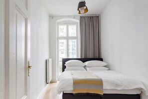 A bedroom with a bed, a radiator, a window with curtains, and a door.