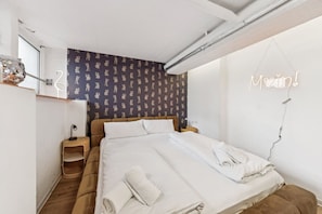 Un dormitorio con una cama, una mesita de noche, una lámpara, un espejo en la pared y un letrero de neón.