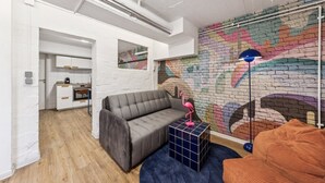 Un soggiorno moderno con un divano grigio, un murale colorato e una cucina sullo sfondo.