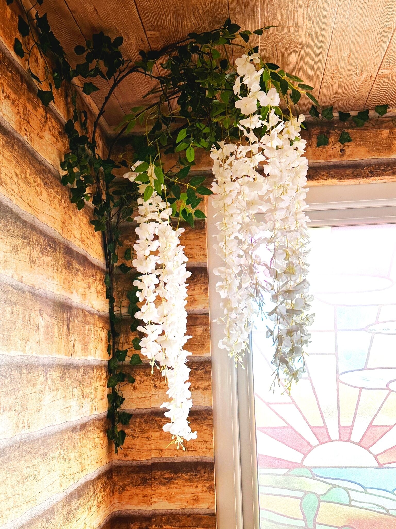 A rustic wooden wall with hanging white flowers and green ivy.
