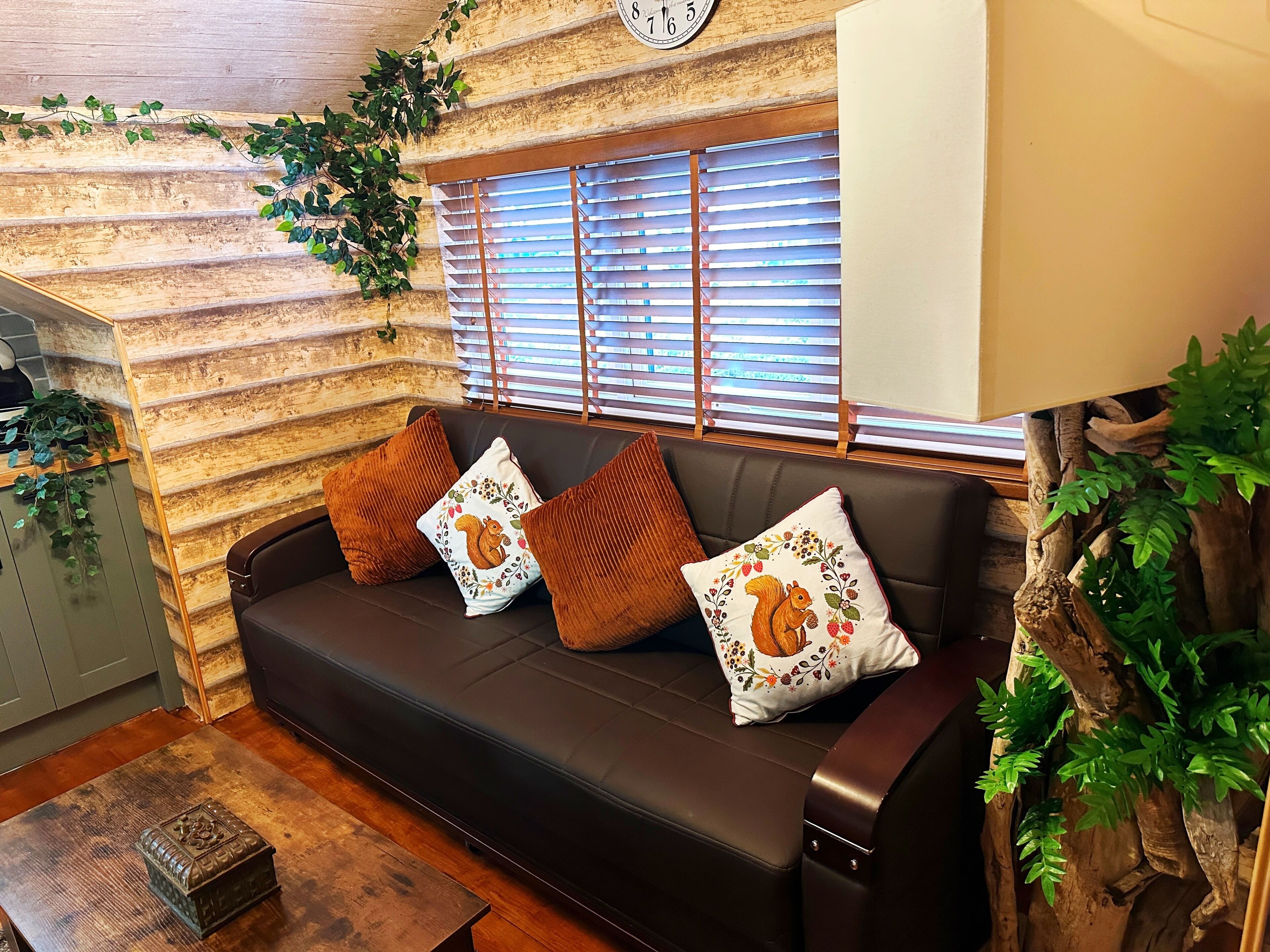 A cozy room with a wooden log wall, a sofa with decorative pillows, a wooden coffee table, and a clock on the wall.