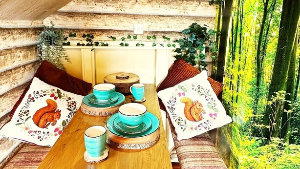 A cozy cabin with a wooden table set for four, surrounded by benches with cushions. - Squirrel Hideaway in Formby, Liverpool (Liverpool)