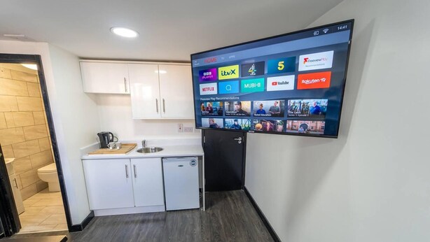 Et moderne køkken med hvide skabe, en indbygget vask og et fladskærms-tv på væggen, der viser forskellige streamingtjenester.