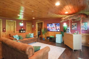 A cozy living room with wooden ceilings, a sofa set, a small refrigerator, and a television.