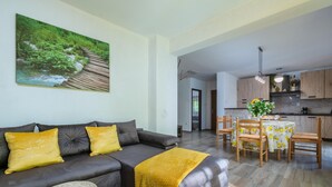 Un salon moderne avec un canapé gris foncé, des coussins jaunes, une petite table ronde et un coin repas comprenant des chaises en bois et une nappe.