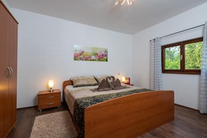 Quarto com cama de madeira, mesa de cabeceira com abajur, pintura de flores na parede e janela com cortinas.