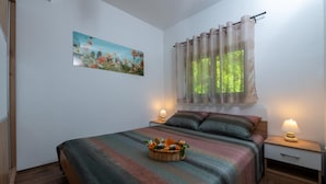 Une chambre à coucher avec un lit, une table de chevet, une lampe, un tableau et une fenêtre avec des rideaux.