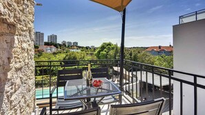 A balcony with a table set for two, overlooking a swimming pool and a cityscape. - Holiday apartment with swimming pool and sun loungers (Pula)