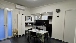 A modern kitchen with white cabinets, a black stove, and a dining area with a table and chairs. - Downtown apartment (Catania)