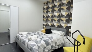 A modern bedroom with a geometric-patterned headboard, a bed with a checkered duvet, a yellow chair, and a black floor lamp. - Downtown apartment (Catania)