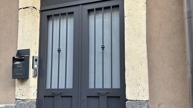 A dark grey double door with a small mailbox and a security camera above it. - Downtown apartment (Catania)