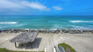 A beach with a thatched umbrella and chairs, a concrete walkway, and a rocky shoreline. - Oceanfront 4BR | Private Beach | 2 Patios | BBQ (Oceanside)