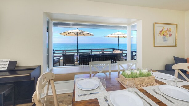 A dining area with a view of the ocean, a piano, and a framed picture on the wall. - Oceanfront 4BR | Private Beach | 2 Patios | BBQ (Oceanside)