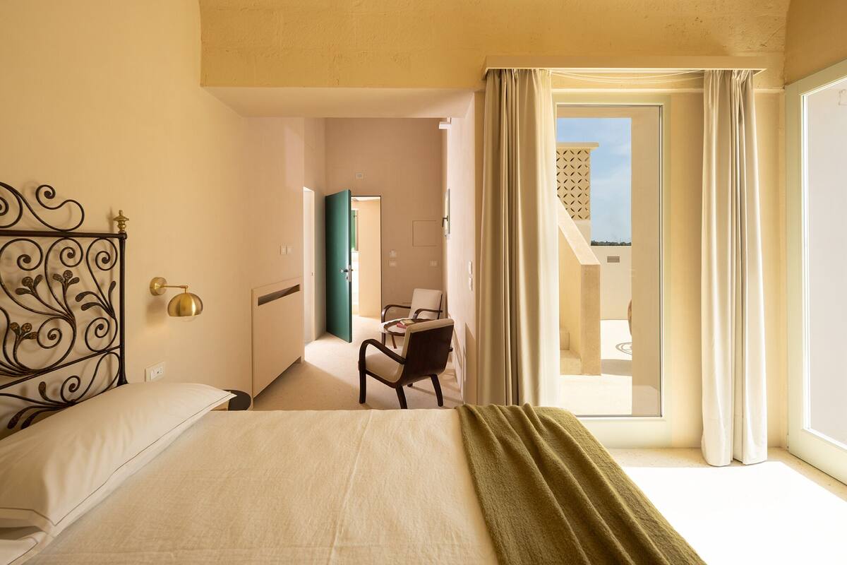 A hotel room with a bed, a desk, and a chair. There is a door leading to a balcony.