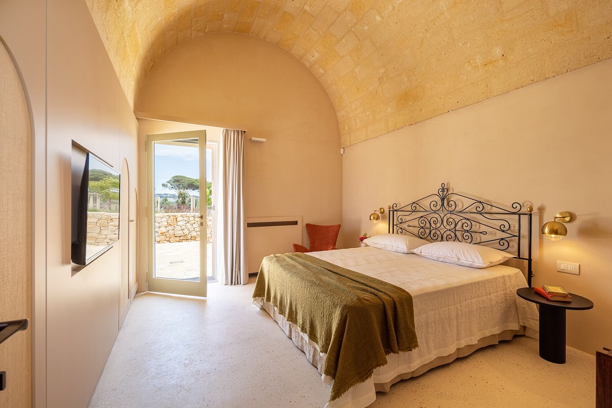 A bedroom with a bed, a nightstand, a TV, and a view of the outdoors.