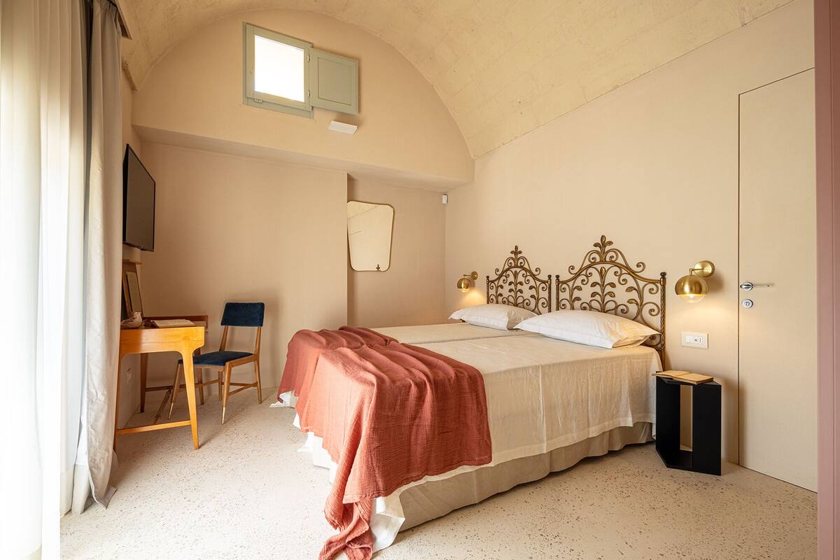 A bedroom with a bed, a desk, a chair, a mirror, and a door.