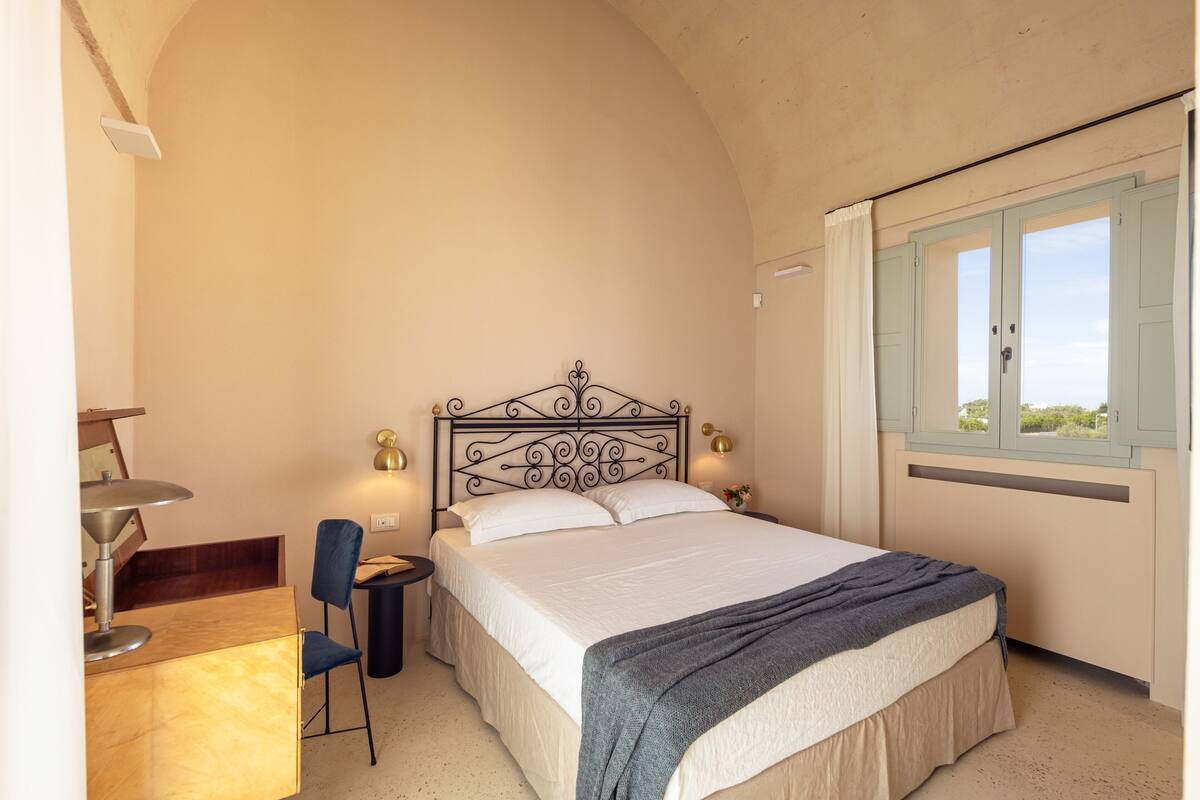 A bedroom with a bed, a desk, a chair, and a window with curtains.