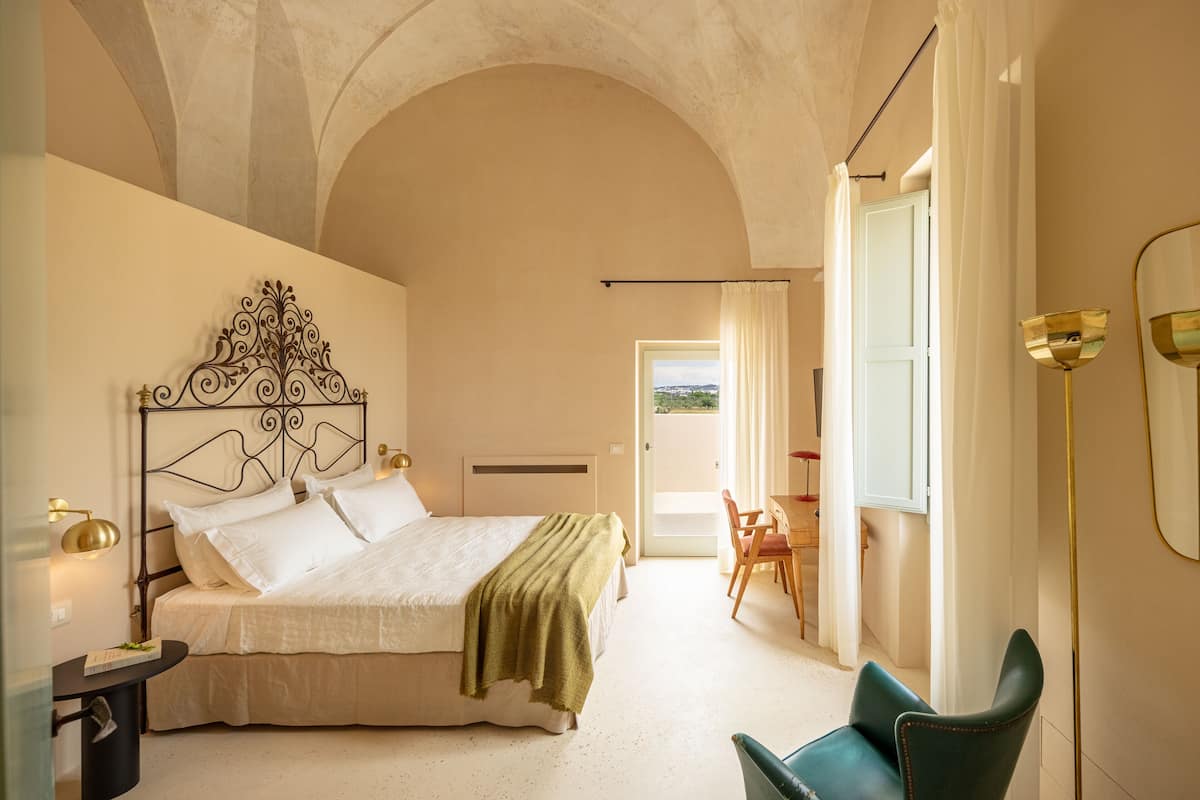 A bedroom with a bed, bedside table, and a view to the outside.