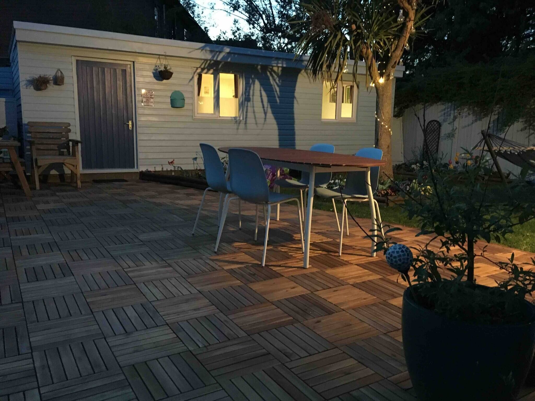 Una terraza de madera con una mesa y sillas, un cobertizo pequeño y una planta en maceta.