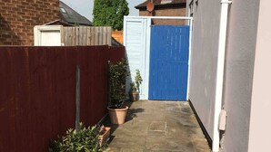 A narrow stone-paved courtyard with a blue gate, a brick wall, and potted plants. - The Beetle Cabin London (Brentford)