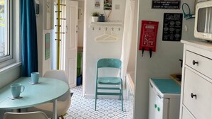 A compact kitchen with a dining area, a small refrigerator, a microwave, and a coffee menu sign. - The Beetle Cabin London (Brentford)