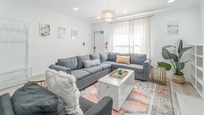 Ein modernes Wohnzimmer mit einem grauen Ecksofa, einem weißen Couchtisch und einem gemusterten Teppich.