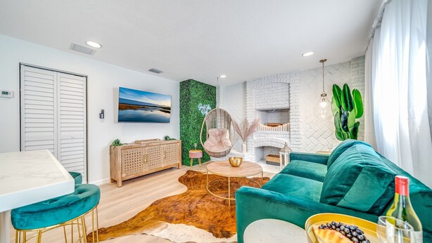 Una sala de estar moderna con un sofá color turquesa, una mesa de centro redonda y un comedor con una mesa blanca y taburetes de bar.