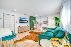 Ein modernes Wohnzimmer mit einem türkisfarbenen Sofa, einem runden Couchtisch und einem Essbereich mit weißem Tisch und Barhocker.
