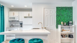 Una cocina moderna con armarios blancos, una isla central con taburetes, un microondas, un lavamanos y una pared verde.