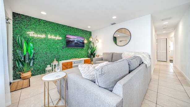Een moderne woonkamer met een groen gestructureerde muur, een grijze bank, een kleine ronde spiegel en een flatscreen televisie.