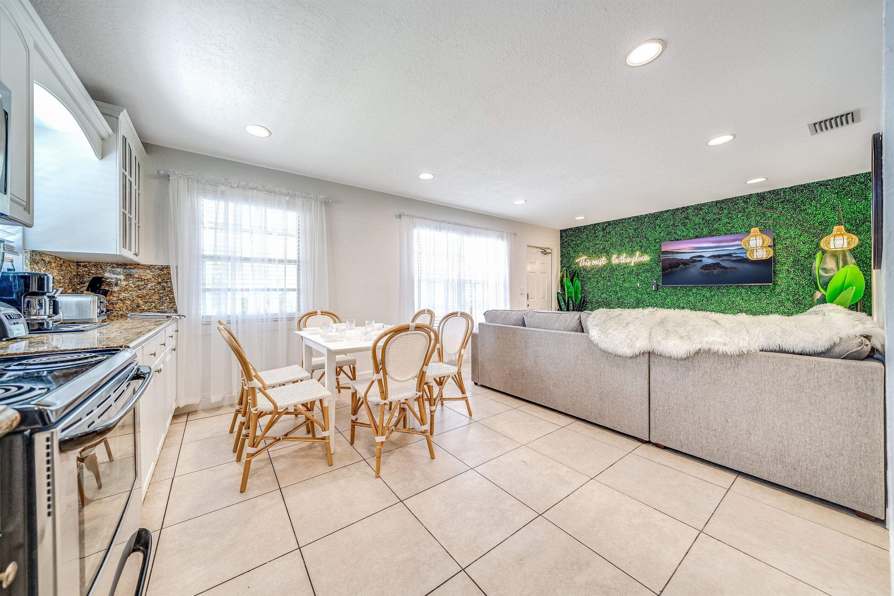 Una cocina moderna con zona de comedor, un sofá con una manta de piel y una pared verde con televisor.