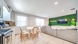 Een moderne keuken met een eethoek, een bank met een bont plaid en een groene wand met een televisie.