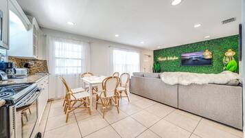 Una cocina moderna con zona de comedor, un sofá con una manta de piel y una pared verde con televisor.