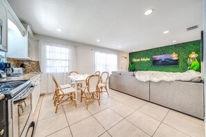 A modern kitchen with a dining area, a sofa with a fur throw, and a green wall with a TV.