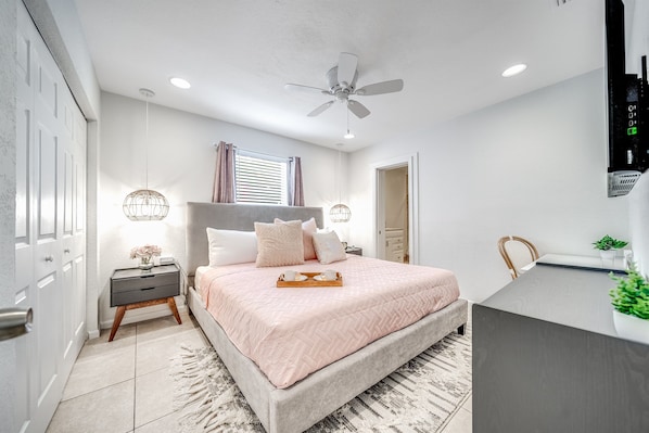 A bedroom with a bed, bedside tables, a ceiling fan, a window with curtains, and a small desk area.