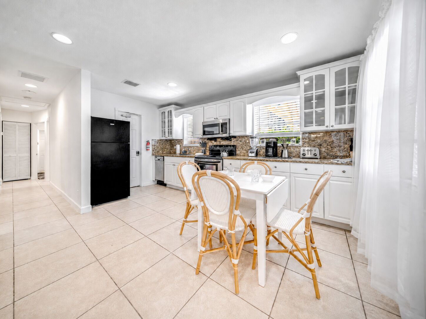 A modern kitchen with white cabinets, a black refrigerator, and a dining area with wicker chairs.