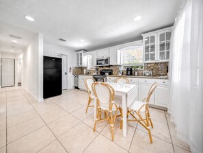 A modern kitchen with white cabinets, a black refrigerator, and a dining area with wicker chairs.