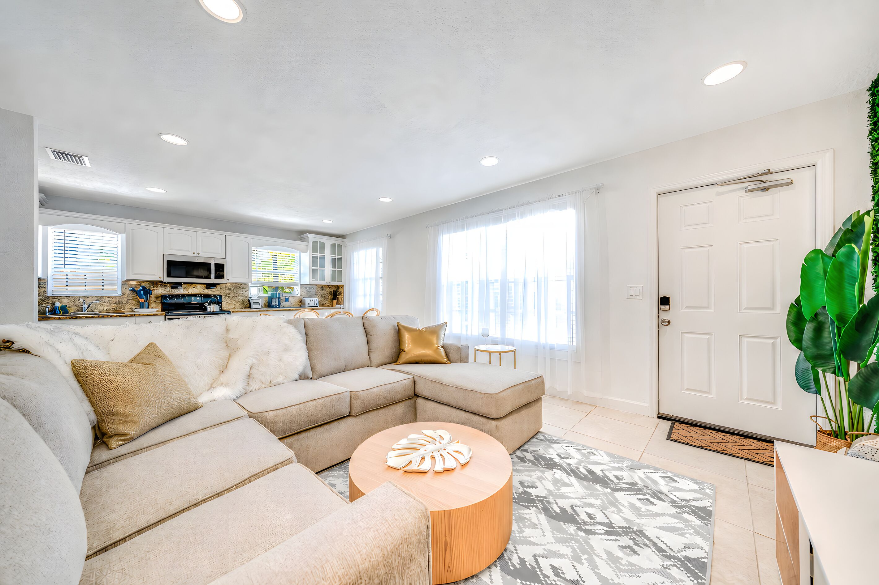 A modern living room with a sectional sofa, a round coffee table, and a kitchen area with a microwave and cabinets.
