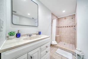 A bathroom with a sink, mirror, potted plant, and shower area.