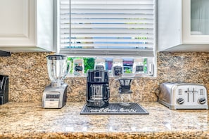 A kitchen with a granite countertop, a coffee maker, a toaster, and a window with blinds.