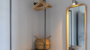 En hall med ett metallställ för kläder, en flätad korg och en stor spegel som reflekterar en dörr och en korg.