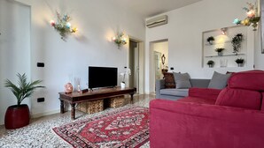 Ein Wohnzimmer mit einem roten Sofa, einem Fernseher auf einem Holzschrank, einem gemusterten Teppich und Wandleuchten.